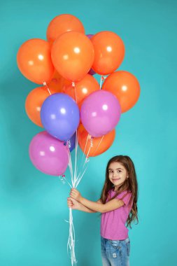 Pembe tişörtlü çocuk renkli balonlarla poz veriyor.