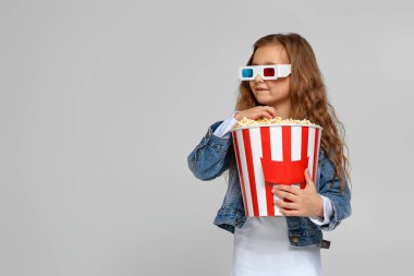 Kırmızı-mavi gözlüklü kız eğleniyor ve elinde patlamış mısır kovası tutuyor.