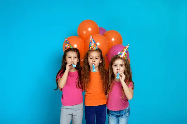 Crianças em chapéu de aniversário com balões de ar coloridos brilhantes soprando chifre de festa — Fotografia de Stock