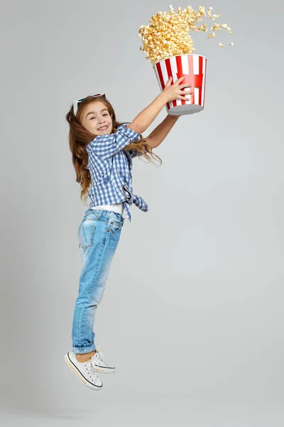 child girl in red-blue 3d glasses holding bucket with flying popcorn