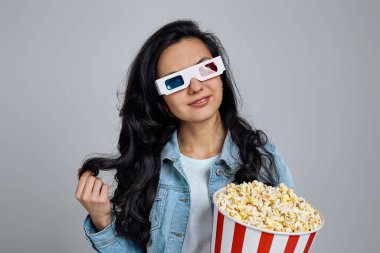 Kırmızı-mavi 3D gözlük takan ve kovadan patlamış mısır yiyen bir kadın.