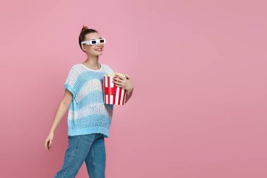 Kırmızı-mavi gözlüklü mutlu bir kadın elinde patlamış mısır kovası tutuyor.