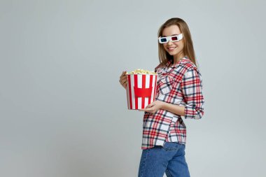 Kırmızı-mavi gözlüklü gülümseyen kadın elinde patlamış mısır kovası tutuyor.