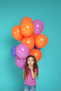 Pembe tişörtlü çocuk renkli balonlarla poz veriyor.