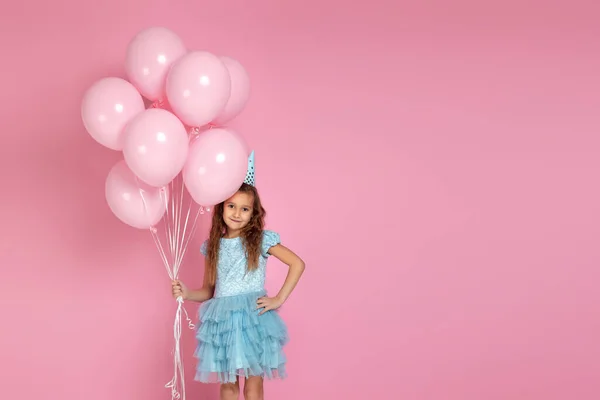 Liten barn flicka i klänning och födelsedag hatt firar med pastell rosa luft ballonger — Stockfoto