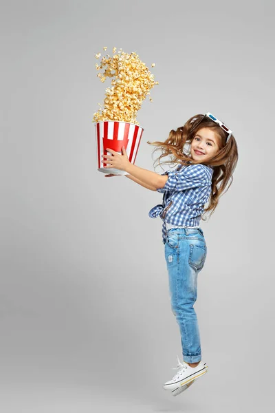 Child girl in red-blue 3d glasses holding bucket with flying popcorn — Stock Photo, Image