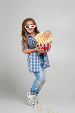 Kırmızı-mavi gözlüklü çocuk elinde patlamış mısır kovası tutuyor.