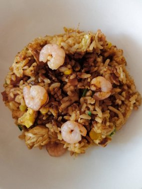 Kızarmış pirinç, karides, mısır, jambon, yeşil soğan, yumurta, tavuk ve soya sosu beyaz tabakta servis edilir.