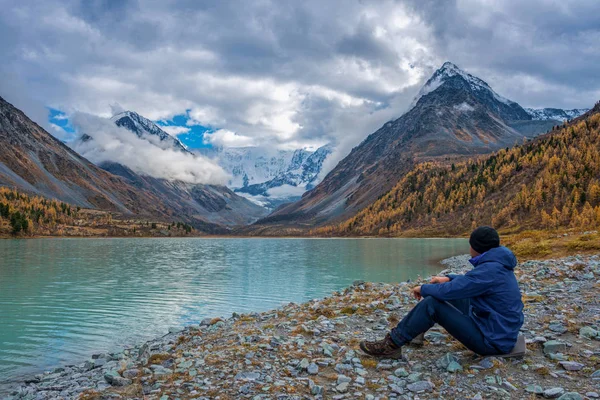 A férfi, aki a tónál ül, és a hegyeket nézi.. — Stock Fotó