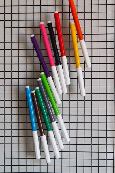 Multi-colored felt-tip pens on a black lattice on a white background