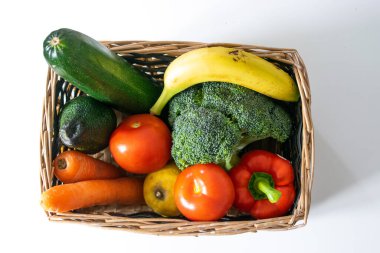 Lezzetli meyve ve sebzelerle dolu rahat bir sepetin fotoğrafı. Brokoli, muz, avokado, kabak, limon, domates, havuç ve biber var. Sıfır atık.
