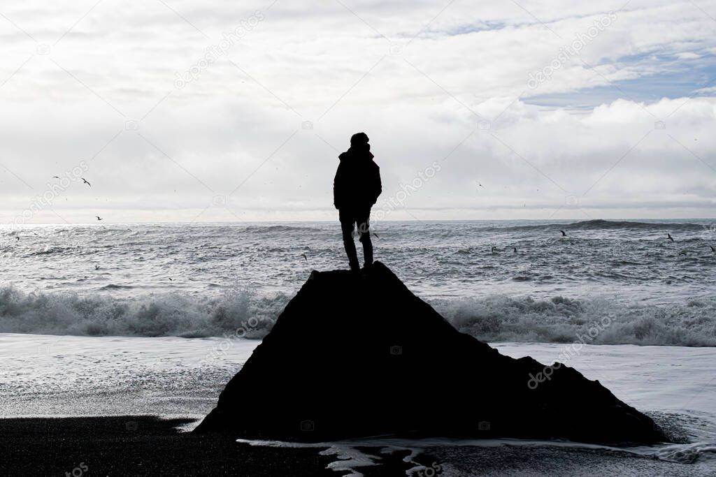 Photo of the silhouette a man standing on a black rock in the black beach in Iceland, Reynisfjara