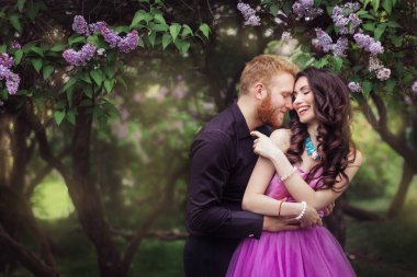 Gelin ve damat leylak ağacının yanında. Birbirine aşık çiftler bahar bahçesinde kucaklaşıyorlar. Boynunda narin bir kolye olan mor kolsuz bir kadın. Siyah takım elbiseli kızıl saçlı adam bir kızı öpüyor ve sarılıyor. Güzel parkta düğün..