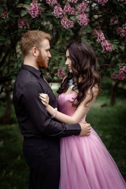 Gelin ve damat leylak ağacının yanında. Birbirine aşık çiftler bahar bahçesinde kucaklaşıyorlar. Boynunda narin bir kolye olan mor kolsuz bir kadın. Siyah takım elbiseli kızıl saçlı adam bir kızı öpüyor ve sarılıyor. Güzel parkta düğün..