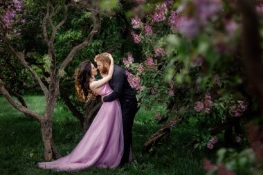 Gelin ve damat leylak ağacının yanında. Birbirine aşık çiftler bahar bahçesinde kucaklaşıyorlar. Boynunda narin bir kolye olan mor kolsuz bir kadın. Siyah takım elbiseli kızıl saçlı adam bir kızı öpüyor ve sarılıyor. Güzel parkta düğün..