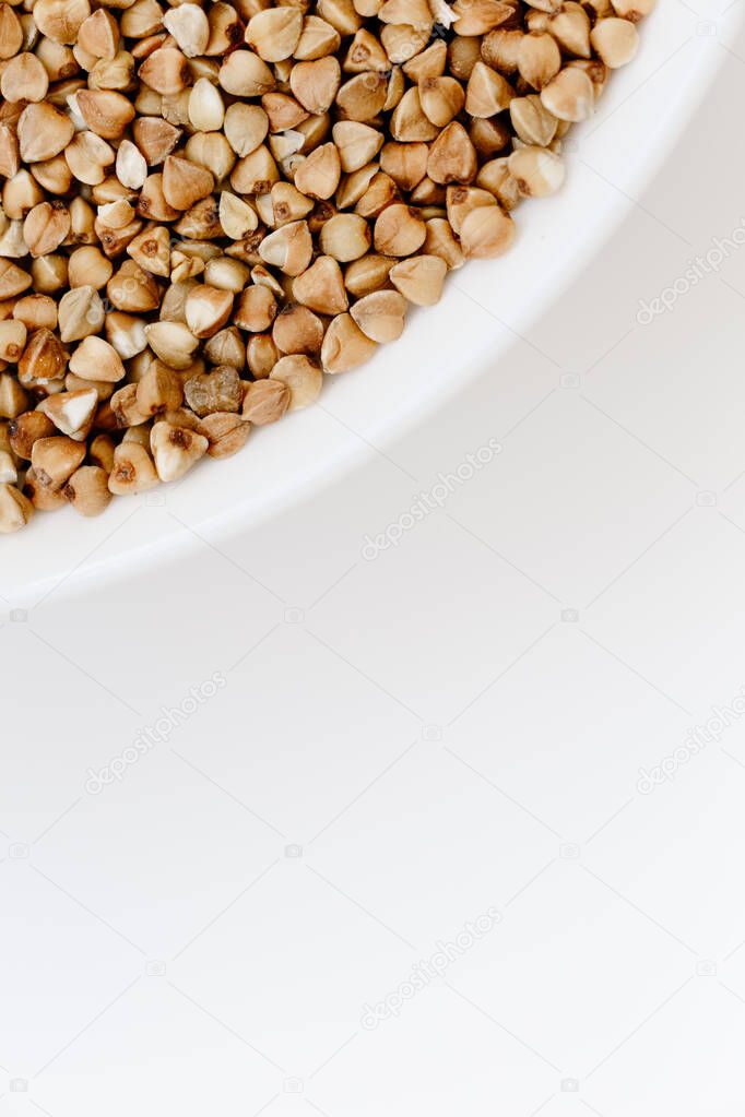 Bowl of uncooked raw buckwheat grains on white isolated background