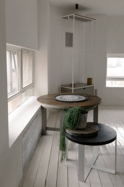 Minimalist ev dekorasyonu: iki şık yuvarlak masa, gri bir duvar, yeşil saksı ev bitkileri, hafif örülmüş pamuk halı.