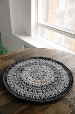 Süslü, minimalist gri İskandinav halısı kahverengi ahşap bir masanın üzerinde yatıyor. Ev yapımı samimi örgü hobisi. Halı dokusu