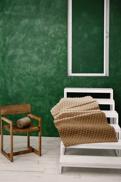 Home composition from everyday objects. A large spool of thread lies on an old vintage chair, a brown beautiful carpet on a white staircase against the background of a green wall. Antique handmade carpet. Isolated home hobby