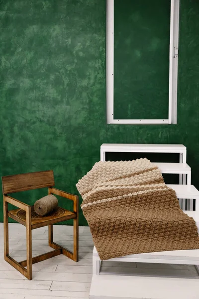 Home composition from everyday objects. A large spool of thread lies on an old vintage chair, a brown beautiful carpet on a white staircase against the background of a green wall. Antique handmade carpet. Isolated home hobby