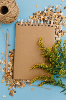 Boş kahverengi klasik defter, yapraklar, sarı çiçekler, iplik yumağı, kalem, kalem, günlük renkli mavi masa. Şık, minimalist iş yeri konsepti. Kopyalama alanı olan üst görünüm.