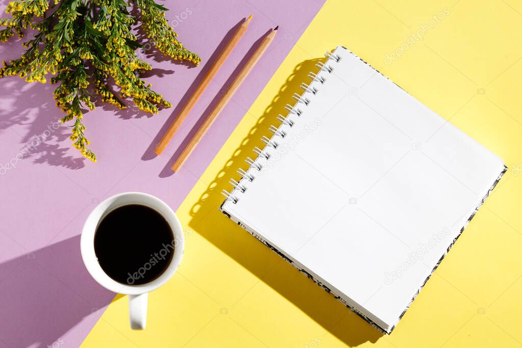 Blank white vintage notebook, leaves, yellow flowers, diary, cup of coffee on purple yellow  background. Minimalistic workplace concept. Top view with copy space. Summer flat lay