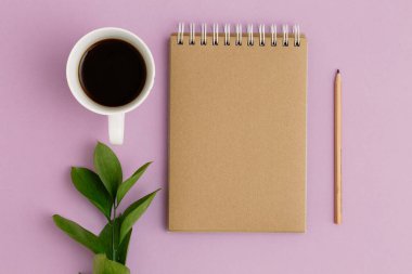 Boş kahverengi klasik defter, yapraklar, sarı çiçekler, kalem, günlük, mor masadaki bir fincan kahve. Şık, minimalist iş yeri konsepti. Kopyalama alanı olan üst görünüm