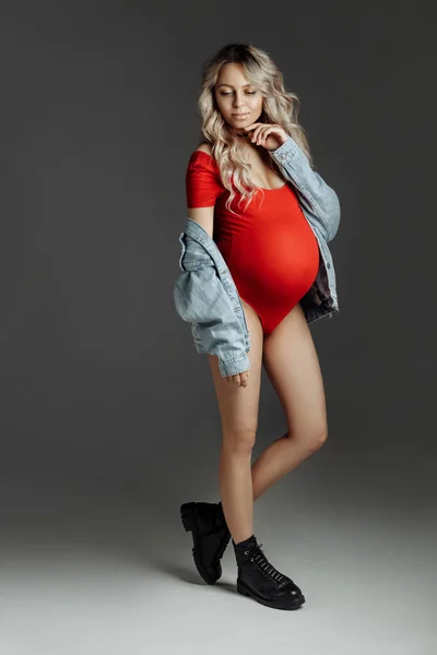 Ung vacker gravid kvinna i röd body suit poserar över grå bakgrund, isolerad. Gravid blond flicka med trendig frisyr — Stockfoto