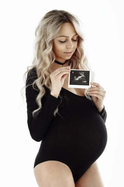 회색 바탕에 격리 된 검은 보디 복을 입은 아름다운 임신 한 행복 한 여성. 초음파를 들고 있는 임신 한 소녀 — 스톡 사진