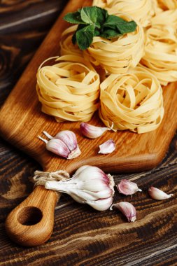 Pişmemiş tagliatelle yuva spagettisi, ahşap bir masada mutfak kesme tahtasında sarımsak. İtalyan Makarnası İçindekiler