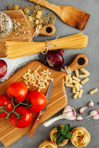 Çimentoda makarna pişirmek için malzemeli spagetti ve fettuccine ile ahşap mutfak tahtası boş, üst manzara. Kırsal tarzda. Soğan, sarımsak, baharat, makarna, domates, bıçak. Düz yatıyordu