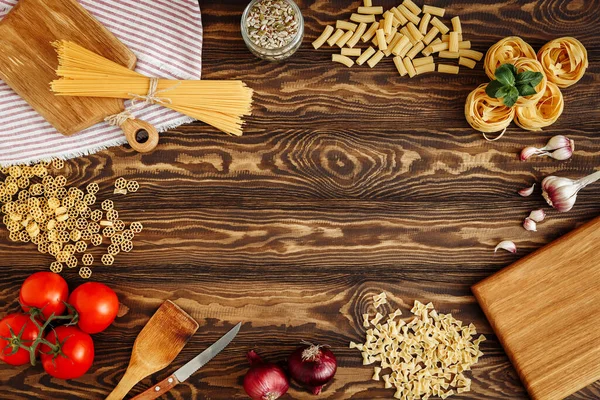 Kırsal tarzda. Düz yatıyordu. İtalyan makarna malzemeleri. Taze sebzeler, baharatlar, kesim tahtası. Kopyalama alanı olan üst görünüm. Tahta masada spagetti ve fettuccine.