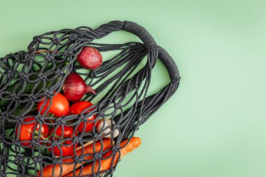 Market tuvali, yeşilde yemek bulunan tel örgü poşeti. Doğal poşetteki sebzeler, çevre dostu, düz zemin. Sürdürülebilir yaşam tarzı konsepti, sıfır atık alışveriş. Plastiksiz, yeniden kullanılıyor, azaltılıyor, geri dönüştürülüyor, reddediliyor