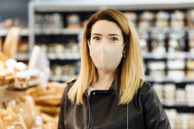 Portrait of a young pretty woman in a protective medical mask who is shopping at the supermarket during a pandemic. The buyer makes purchases at the grocery store. clipart