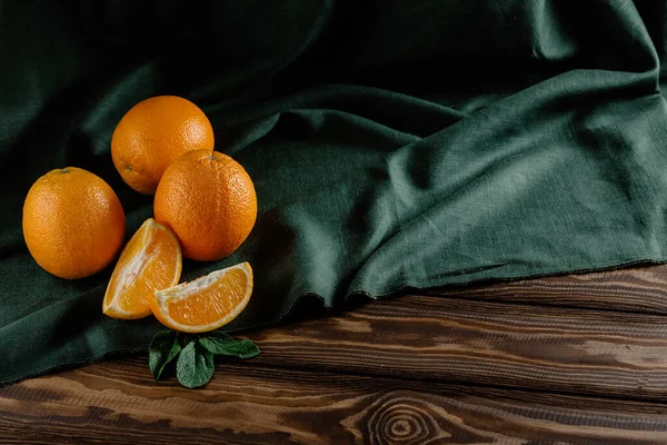 Ολόκληρα Και Κομμένα Πορτοκάλια Δίπλα Ένα Πράσινο Λινό Τραπεζομάντηλο Πάνω — Φωτογραφία Αρχείου