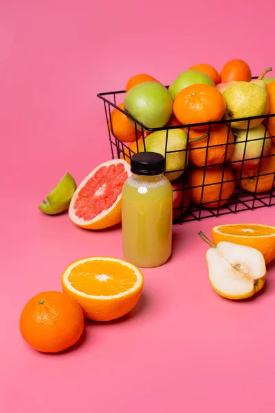 meyve suyu şişesi ve meyve sepeti pembe arka planda, meyve dağınık