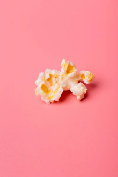 Bir patlamış mısır tanesi pembe arka planda yatıyor.