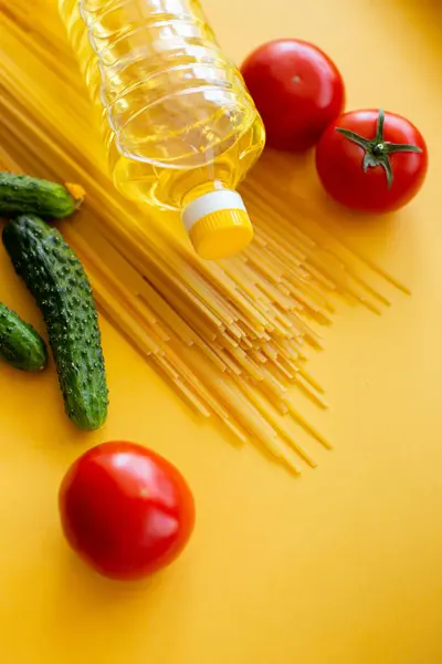 Spagetti, yağ şişesi, salatalık, domatesler sarı arka planda.