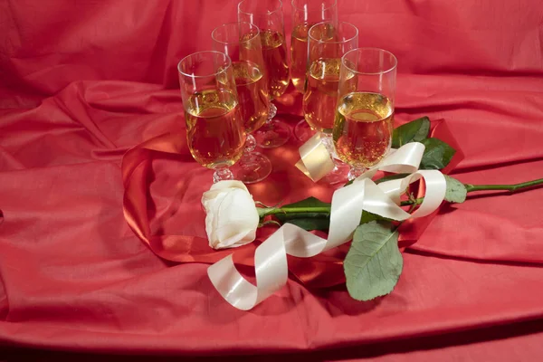 红色的背景是六杯香槟 内装一条红丝带和一朵白玫瑰 — 图库照片