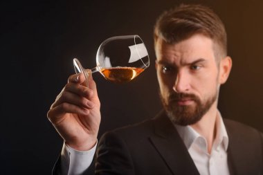 Bir içecek tatma işlemi. Bir şarap stuart yarısı dolu bardak brendi holding ve içki yapısını bakıyor. Siyah arka plan ve turuncu arka ışık ile atış stüdyo.