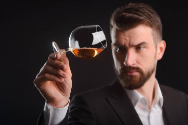 Sommelier bir içecek test. Sakallı bir adam kaldırdı ve bir bardak konyak kendi tarafında tilts. Güzel yatay siyah arka plan ile vurdu.