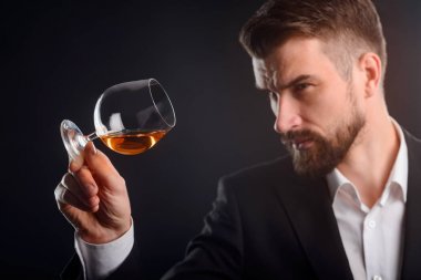Sommelier şarap kalitesini değerlendirmek. Genç adam viski bardağını kendi tarafında eğilme ve gözleri daha içecek görünümü ayrıntılı daralmış. Bir cam seçici odaklı stüdyo vurdu.
