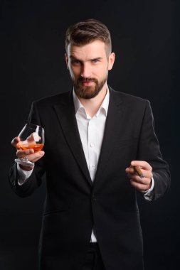 Bardak konyak tutan ve bir puro sigara beyefendi. Adam alkollü içecekler ve tütün içme karanlık bir odada bir dinlenme sahip yükseltilmiş kaş ile çekici. Portre siyah arka plan ile.