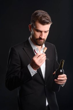 Profesyonel tatma kırmızı şarap. Bu genç adam sadece koyu yeşil bir şişe şarap ve cork adlı arayan açtı. Sommelier dikey çekim resmi elbise, siyah arka planda giyinmiş.