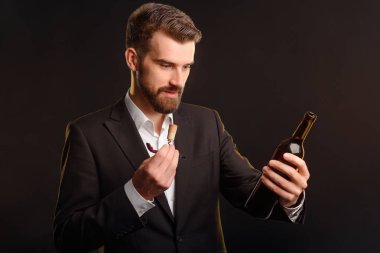 Açılan şişe şarap Professional'la. Cork bir sommelier bıçakla tutarak ve koyu yeşil şişe arıyorum sağlam görünümü olan bir adam. Yatay studio ile koyu arka plan vurdu.