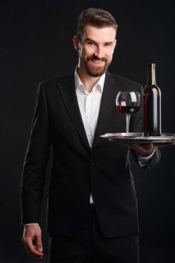 Şarap ile uzman taşıma tepsi. Sakallı adam resmi kıyafeti giymiş bir bardağı ve bir şişe şarap his üzerinde tutan geniş bir gülümseme. Sommelier siyah heybetli dikey fotoğraf.