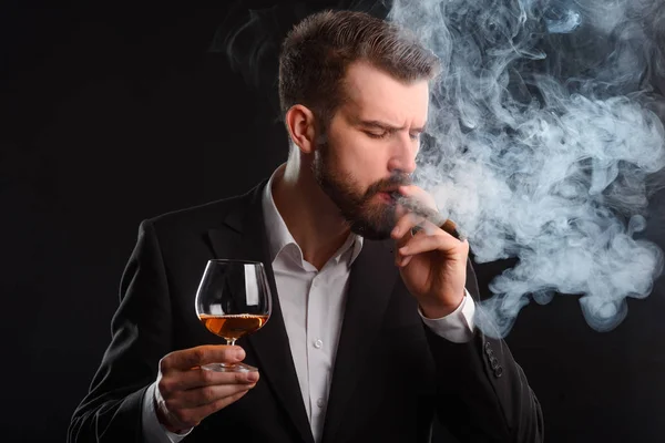 Businessman smoking and drinking brandy. A man in expensive suit inhaling a cigar and blowing much smoke and holding a half-full glass of Scotch.
