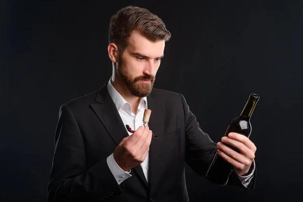 Restaurant worker and wine bottle. Photo of wine steward holding opened bottle and its cork in hands. Horizontal orientation, black background.