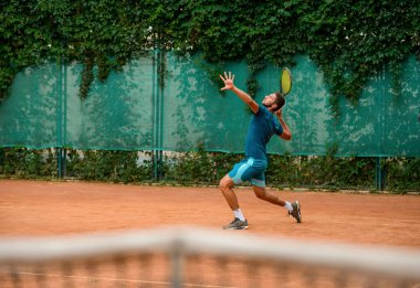 Tenisçi servis atışı yapmak için raket sallıyor..