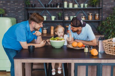 Küçük kız eşcinsel ailelere aşçılık becerilerini gösteriyor ve salata pişiriyor.